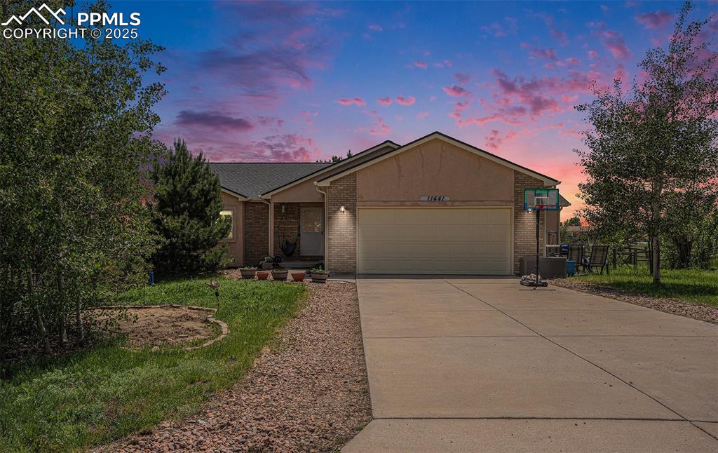 Caption: Ranch-style house featuring a garage, driveway, and brick siding