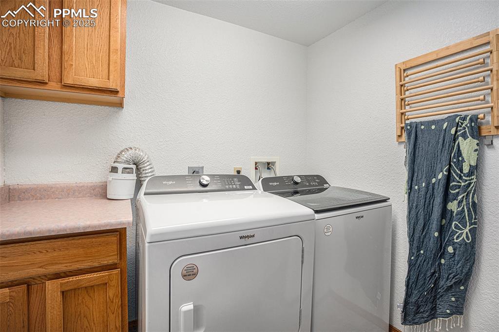 Image 19 of 27: Washroom with cabinet space, washer and clothes dryer, and a textured wall