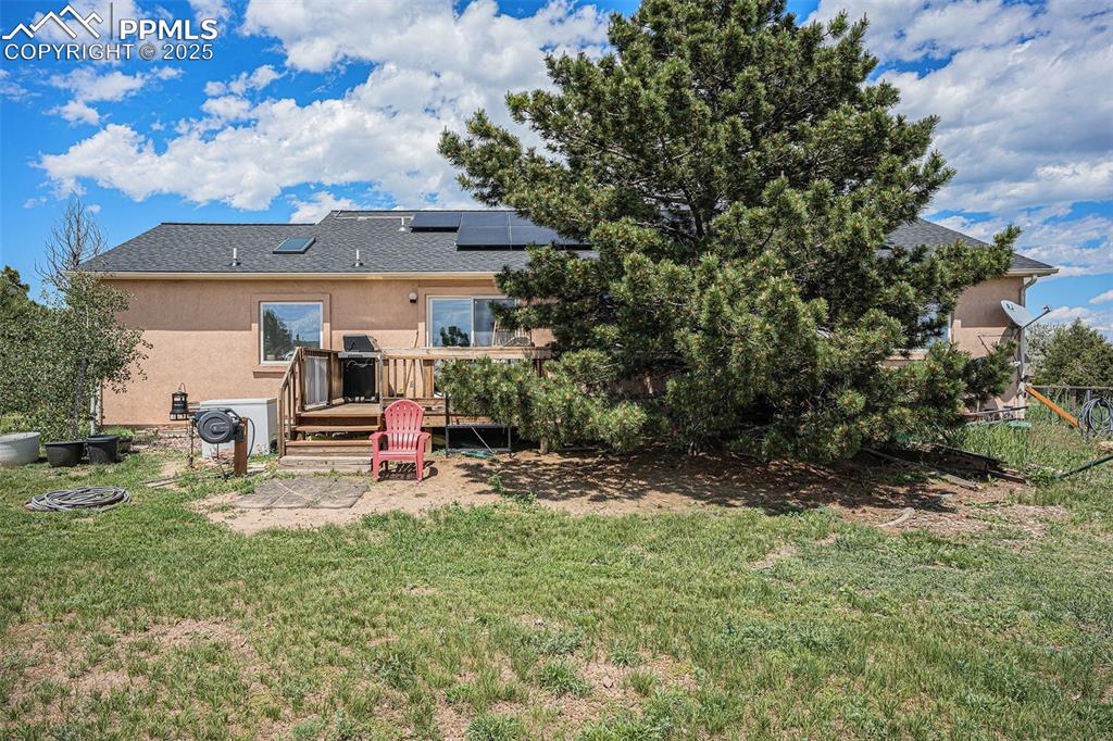 Image 22 of 27: Back of property featuring stucco siding, a deck, a yard, roof mounted sola