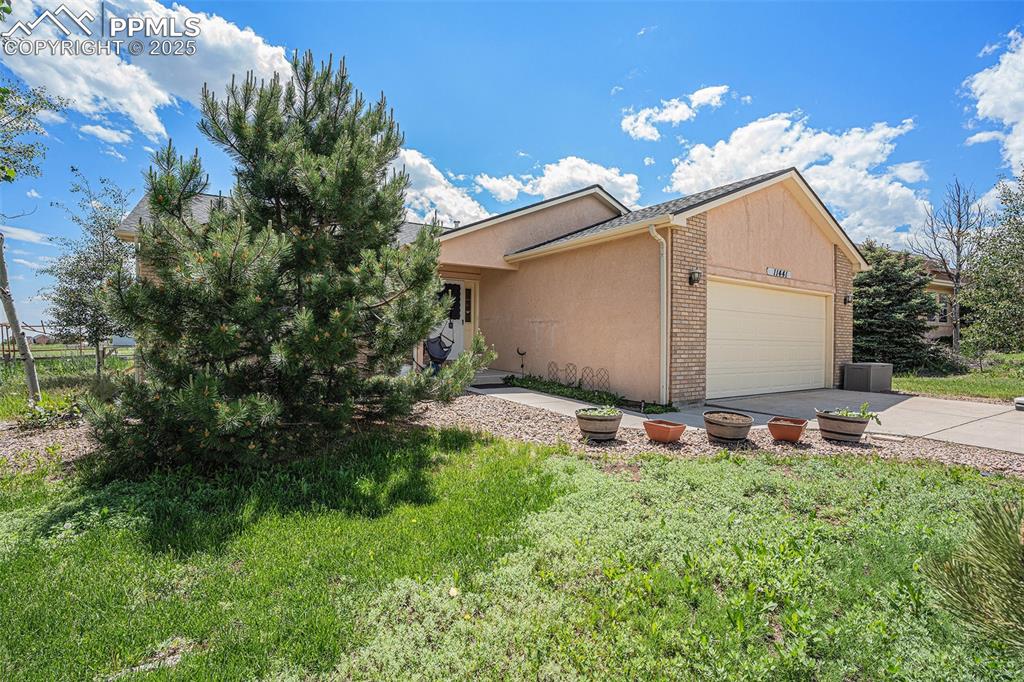 Image 27 of 27: View of side of home featuring a garage, stucco siding, driveway, and brick