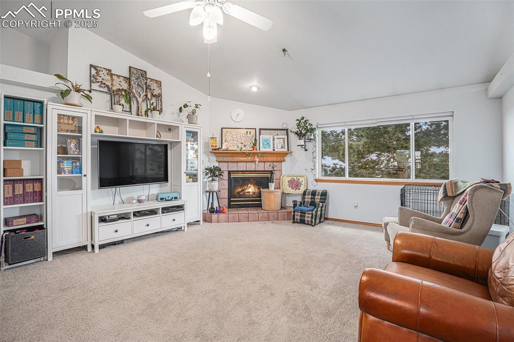 Image 6 of 27: Carpeted living area with vaulted ceiling, ceiling fan, and a fireplace