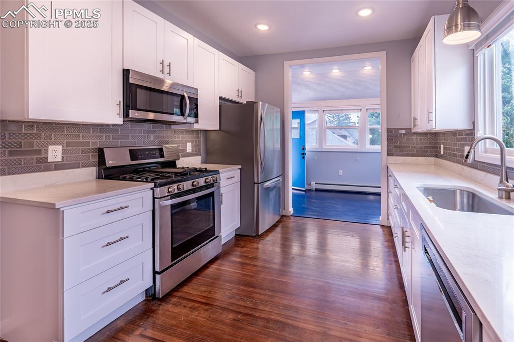 Image 13 of 49: Kitchen featuring backsplash, stainless steel appliances, white cabinets, d