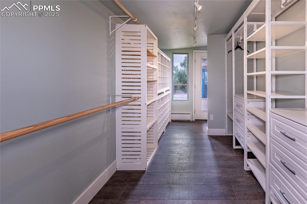 Image 20 of 49: Spacious primary closet with a baseboard radiator and dark wood-style floor