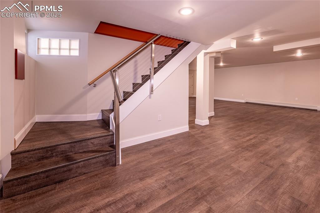 Image 23 of 49: Basement with baseboard heating, stairway, and dark wood finished floors