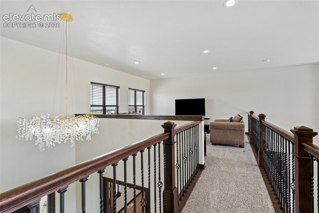 Image 23 of 46: Upper-level hallway featuring a decorative chandelier, dark wood railings w