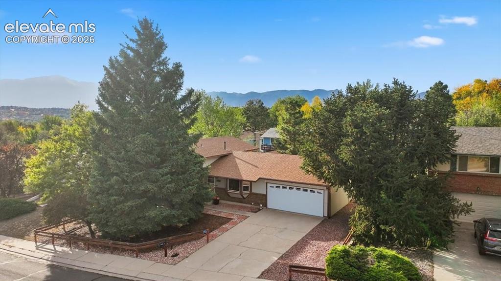 Caption: Ranch-style residence featuring a prominent garage, a concrete driveway, and mature landscaping