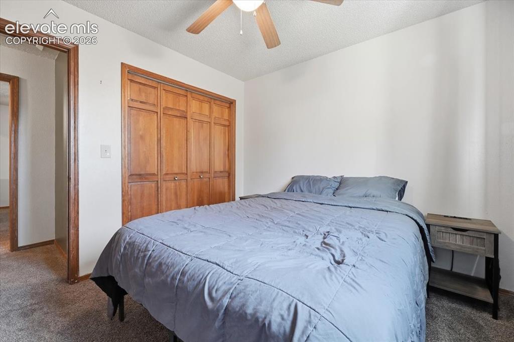 Image 10 of 25: Wood-finish bi-fold closet doors, textured ceiling, and a ceiling fan