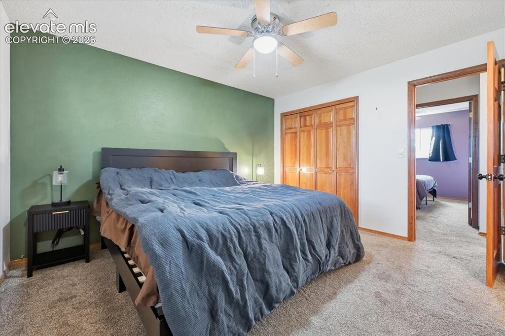 Image 12 of 25: Carpeted bedroom featuring a ceiling fan with light, wood-finish bi-fold cl