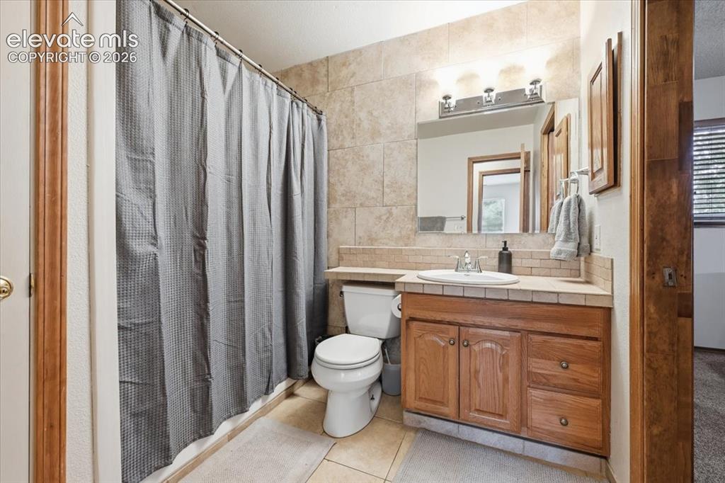 Image 13 of 25: Tile flooring, tile shower surround, wood-finish vanity, integrated sink, a