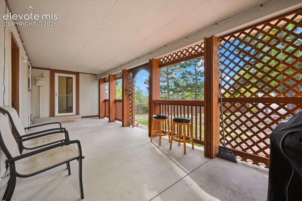 Image 21 of 25: Covered patio featuring an exterior entry door, concrete flooring, and latt