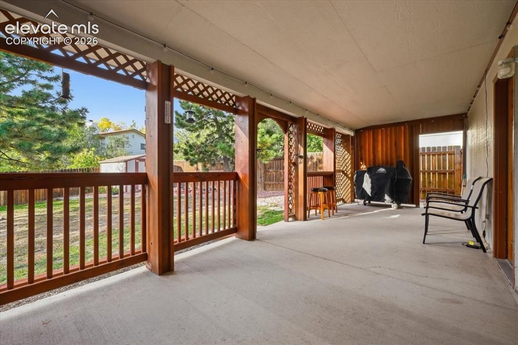 Image 22 of 25: Covered patio with a concrete surface, wood-finish railing, and lattice acc