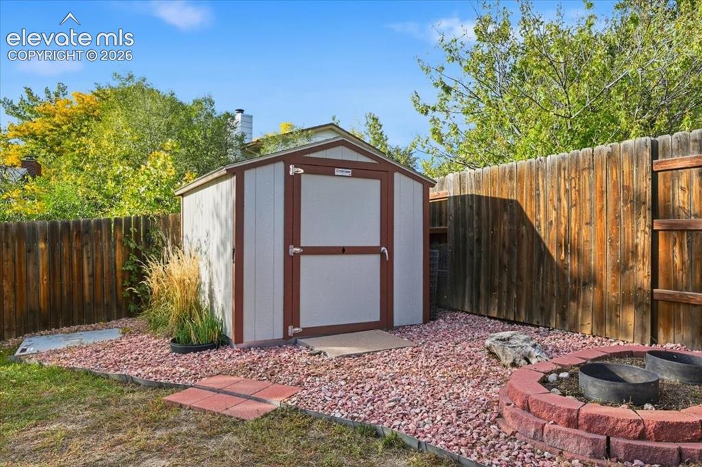 Image 23 of 25: Freestanding storage shed with wood-finish siding, positioned on a red grav