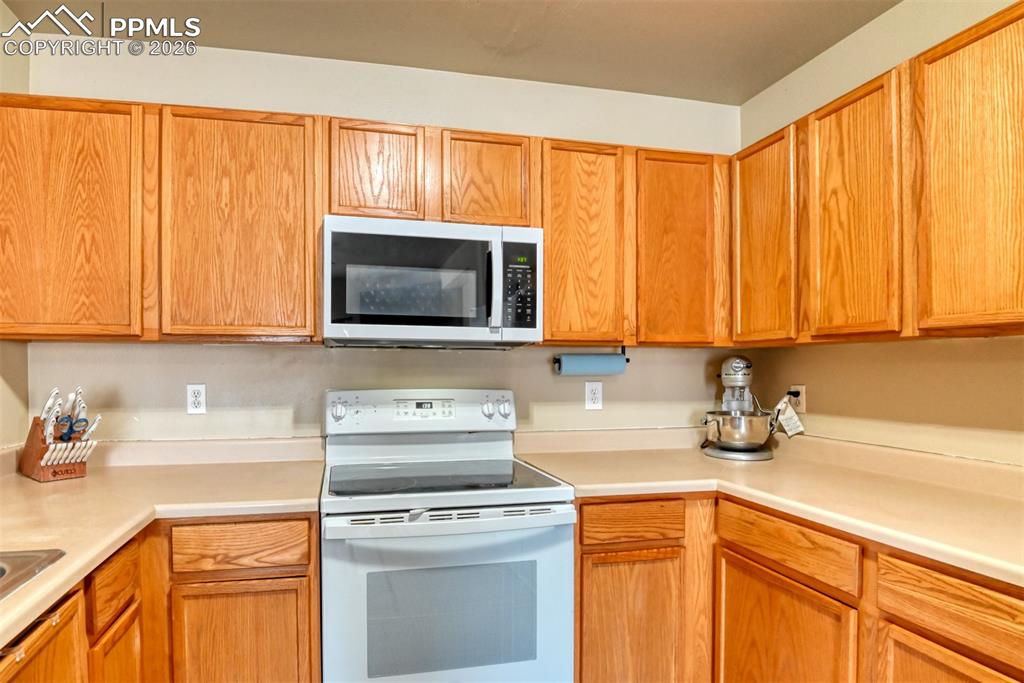 Image 12 of 35: Kitchen with white electric stove, light countertops, and wood finish cabin