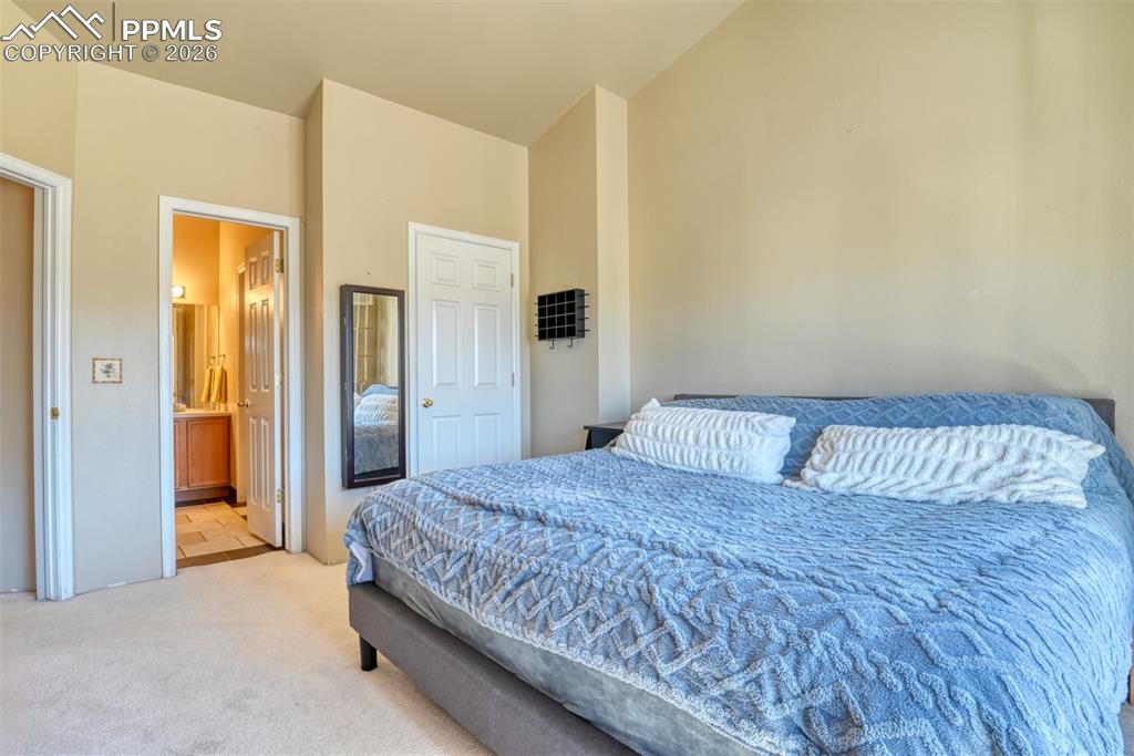 Image 25 of 35: Bedroom with light carpet, ensuite bath, and lofted ceiling