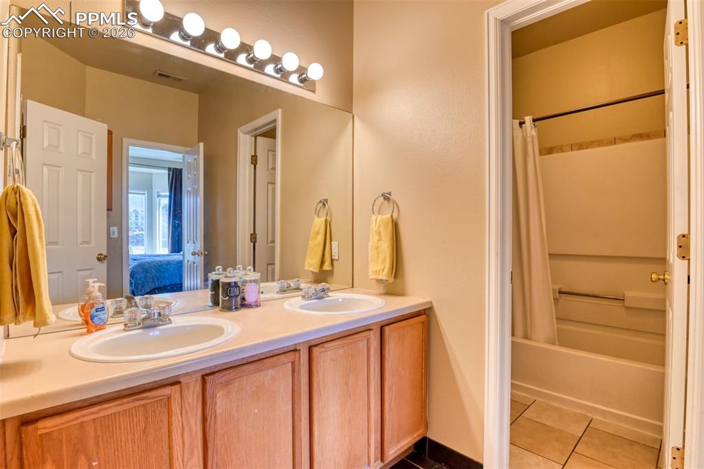Image 28 of 35: Bathroom featuring double vanity, connected bathroom, dark tile patterned f