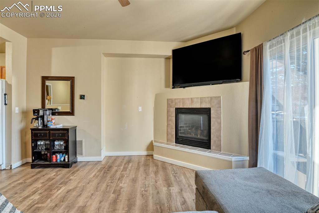 Image 4 of 35: Living area featuring a tile fireplace, ceiling fan, and light wood-type fl