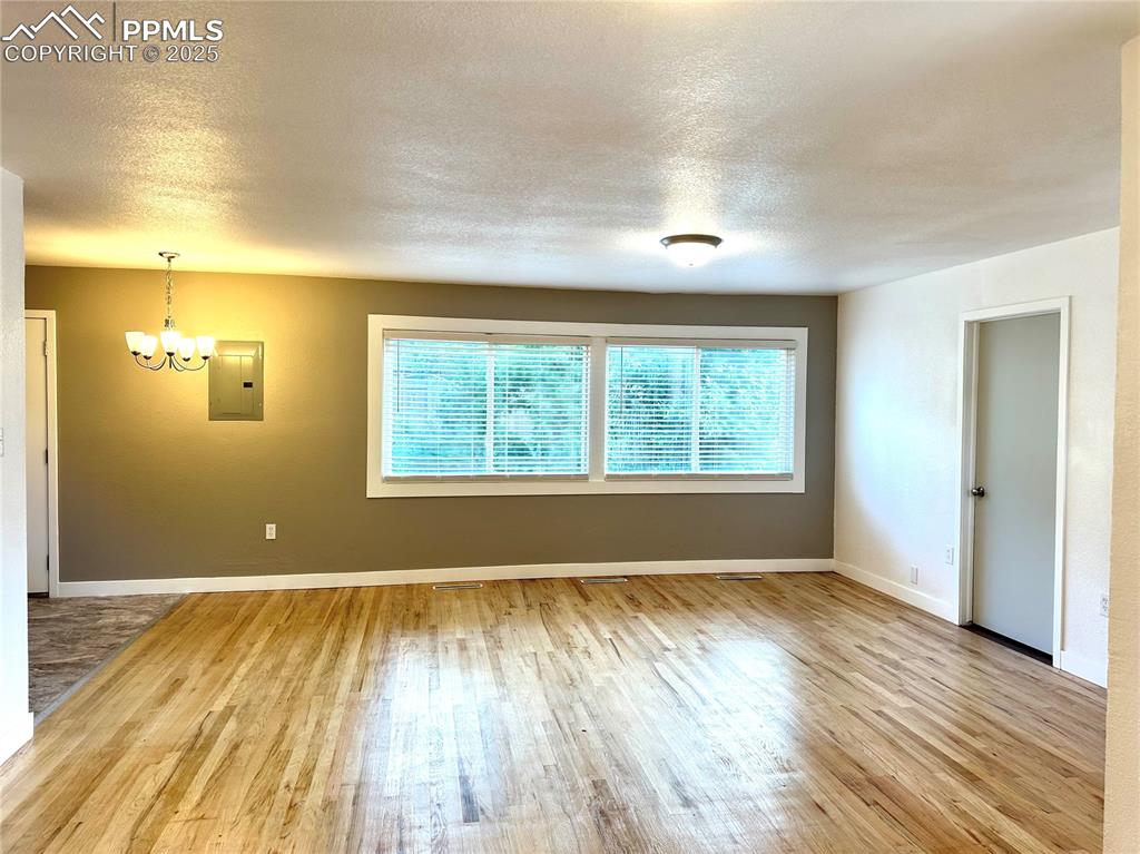 Image 2 of 9: Unfurnished room with electric panel, wood finished floors, a chandelier, a