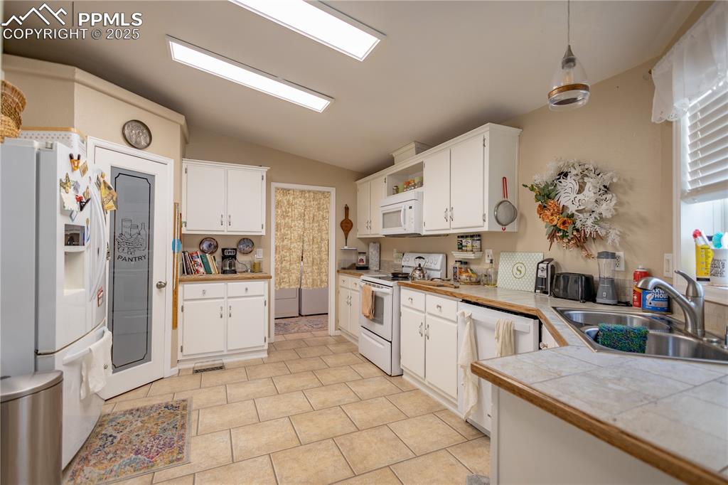 Image 16 of 19: Kitchen with vaulted ceiling, white appliances, and white cabinetry