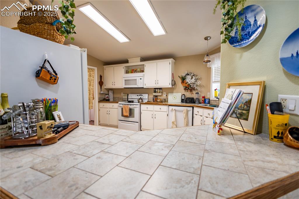 Image 17 of 19: Kitchen with white appliances, white cabinetry, pendant lighting, and tile 