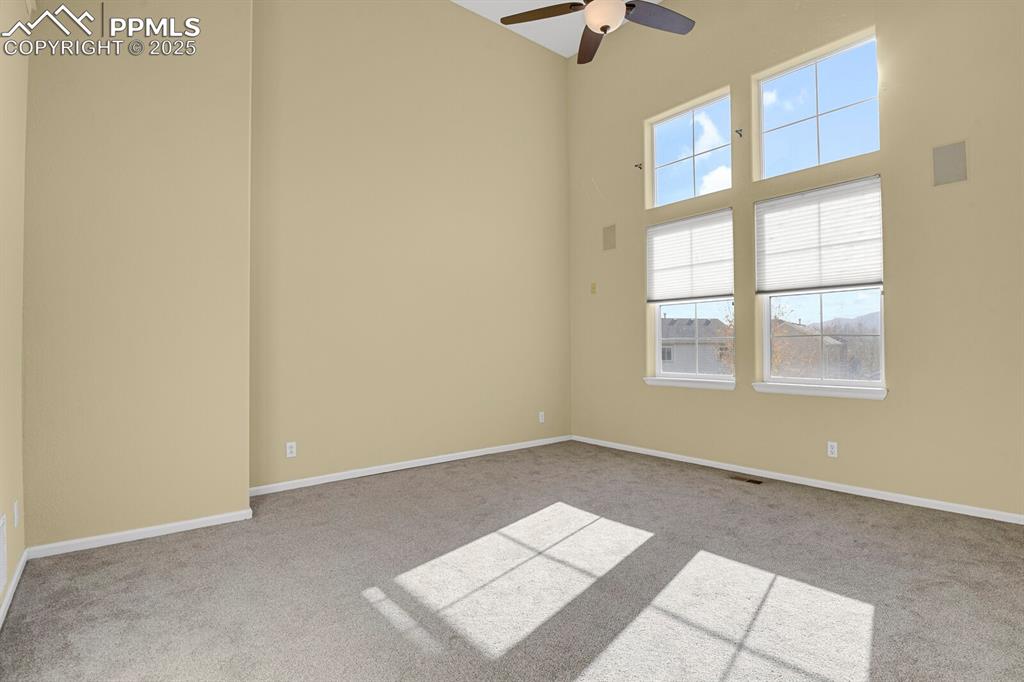 Image 17 of 45: Empty room with light colored carpet, a high ceiling, and a ceiling fan