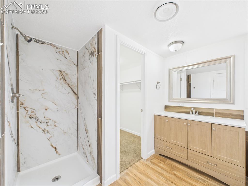 Image 17 of 34: Full bathroom with wood finished floors, a marble finish shower,  vanity