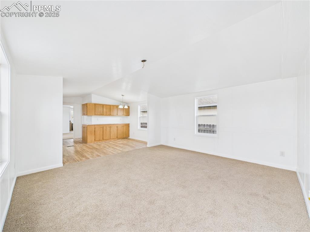 Image 3 of 34: Unfurnished living room featuring light carpet, baseboards, and vaulted cei