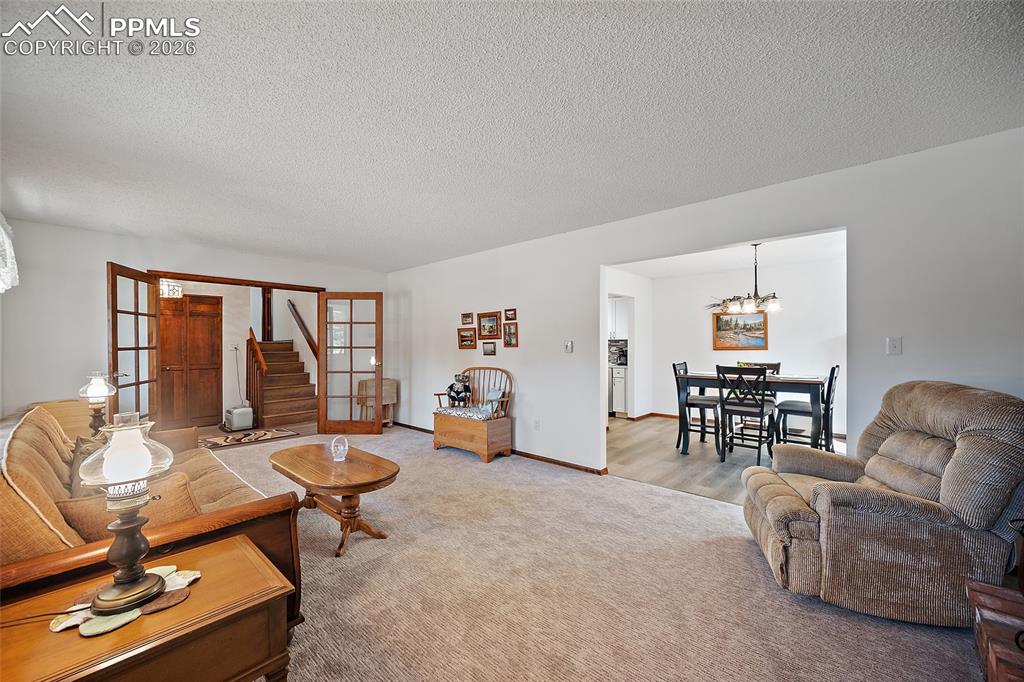Image 14 of 49: Spacious living room with French doors and brick fireplace opens to the for
