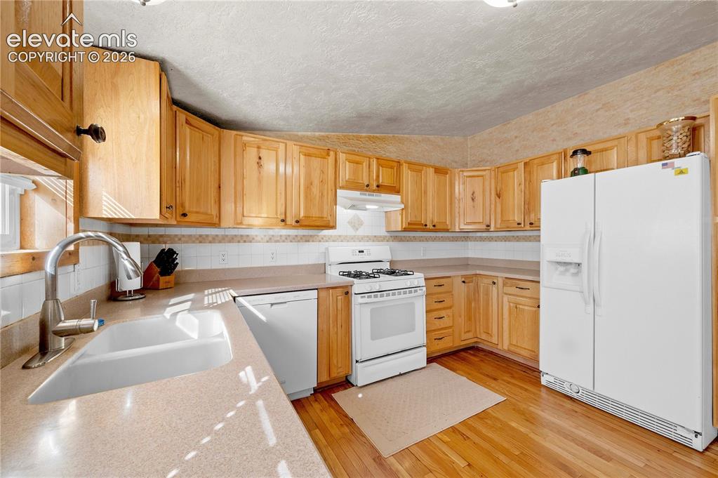 Image 12 of 48: Kitchen with sink, vaulted ceiling, light wood-type flooring, a textured ce