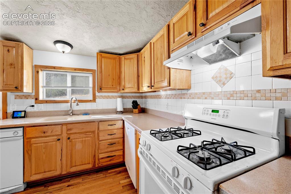 Image 13 of 48: Kitchen featuring backsplash, sink, light wood-type flooring, a textured ce