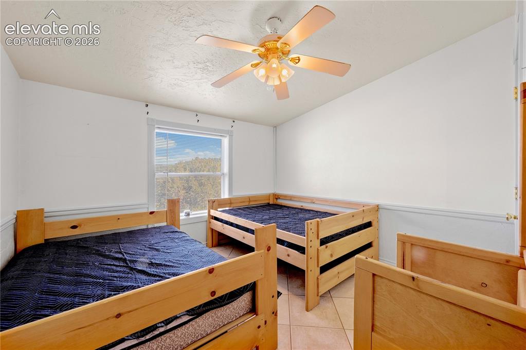 Image 15 of 48: Tiled bedroom with ceiling fan and a textured ceiling