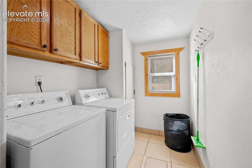 Image 21 of 48: Clothes washing area featuring cabinets, a textured ceiling, light tile pat