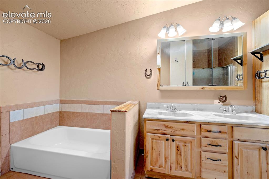 Image 27 of 48: Bathroom featuring tile walls, vanity, separate shower and tub, and a textu