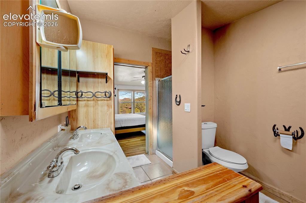 Image 28 of 48: Bathroom with a textured ceiling, an enclosed shower, toilet, tile patterne