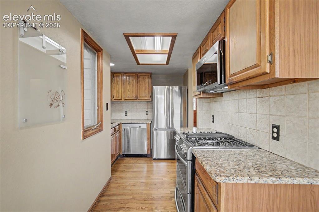 Image 17 of 44: Galley kitchen featuring wood cabinetry, stainless steel appliances, speckl