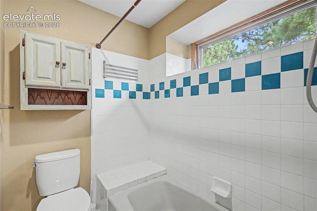 Image 30 of 44: Bathroom featuring white ceramic tile shower surround with a checkerboard a