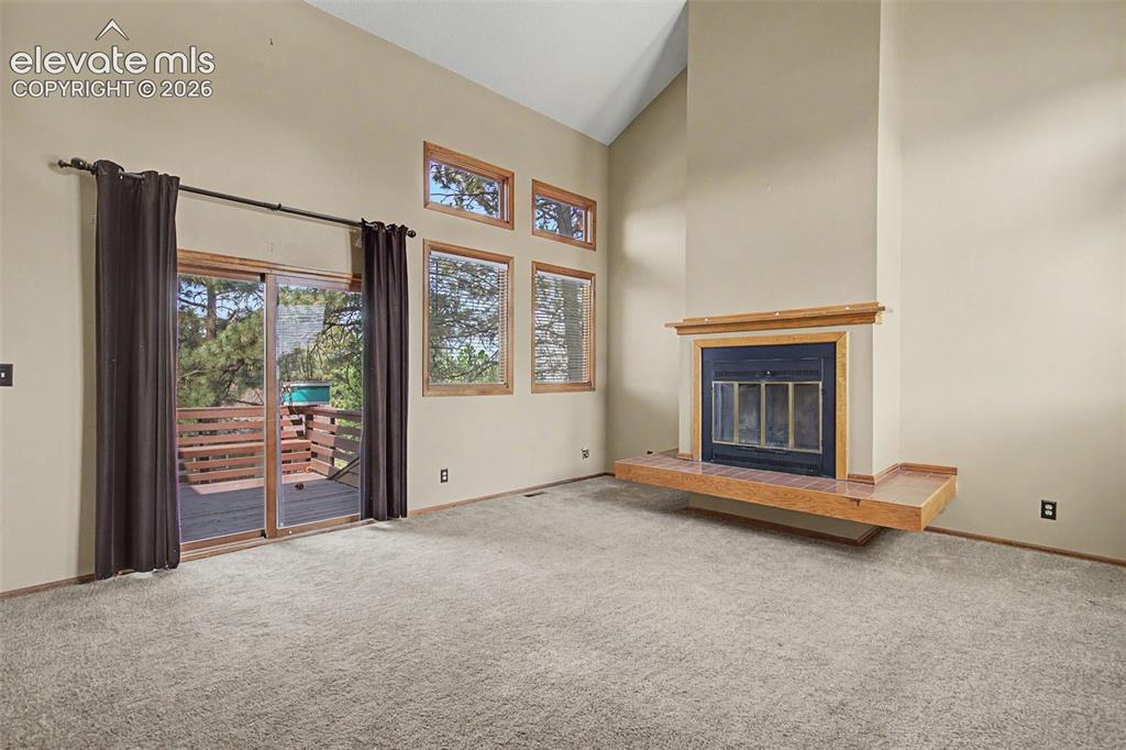 Image 6 of 44: Living area featuring a fireplace with a wood mantle and hearth, high vault