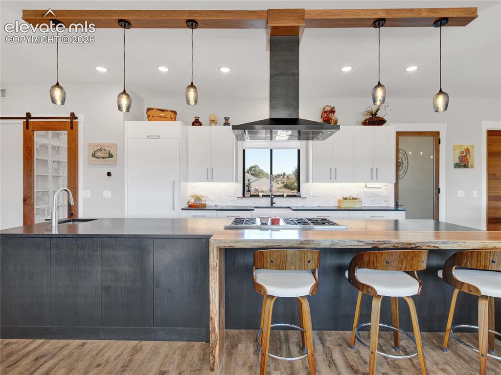 Image 11 of 49: Modern kitchen featuring a large island with dark cabinetry and a wood-fini