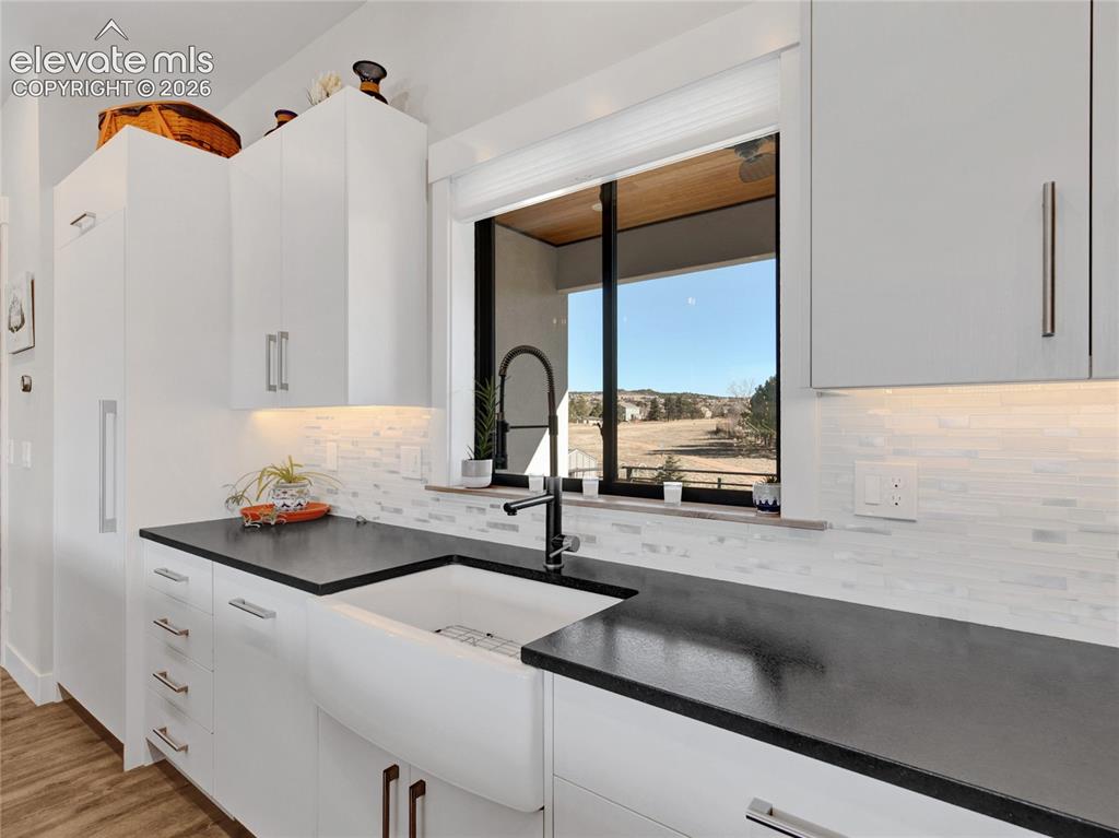 Image 13 of 49: Modern kitchen featuring white cabinetry, dark countertops, a white farmhou