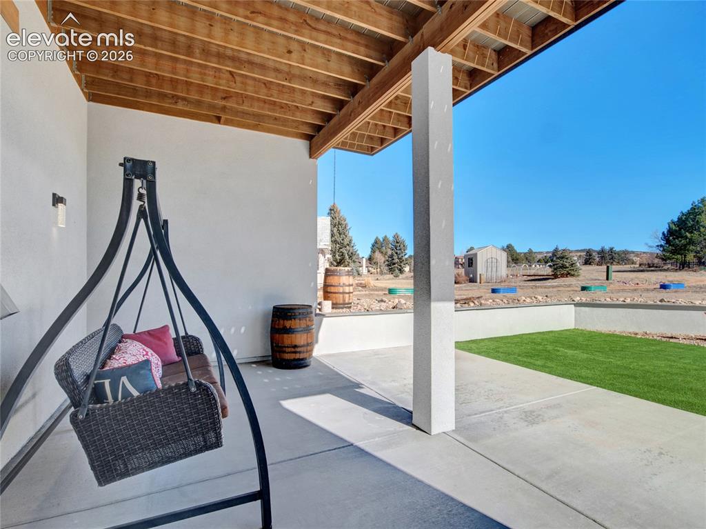 Image 34 of 49: Covered patio with concrete flooring, exposed wood ceiling beams, a white s