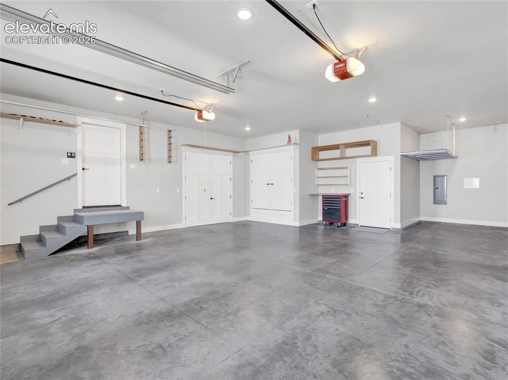 Image 39 of 49: Spacious garage with durable concrete flooring, multiple overhead lighting