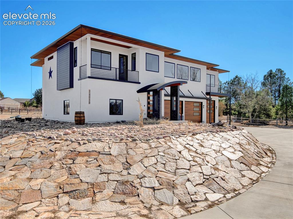 Image 44 of 49: Contemporary stucco exterior featuring a stone retaining wall, oversized wi