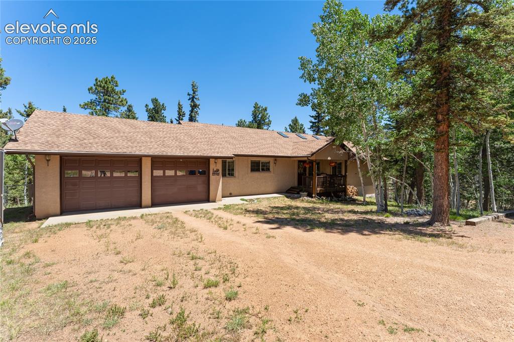 Image 1 of 43: Ranch-style exterior with a two-car garage, covered porch, and mature trees