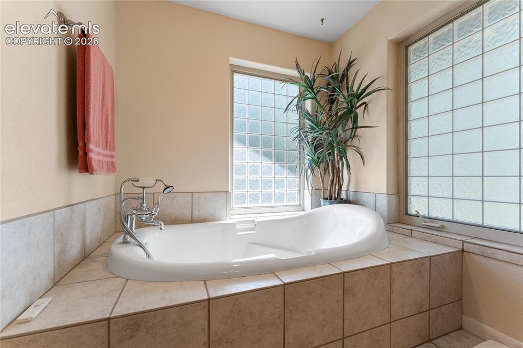 Image 12 of 43: Soaking tub set within a tiled surround, featuring a chrome faucet with a h