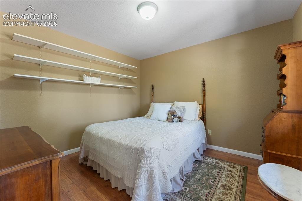 Image 17 of 43: Bedroom with wood-finish flooring, neutral wall paint, and white baseboards
