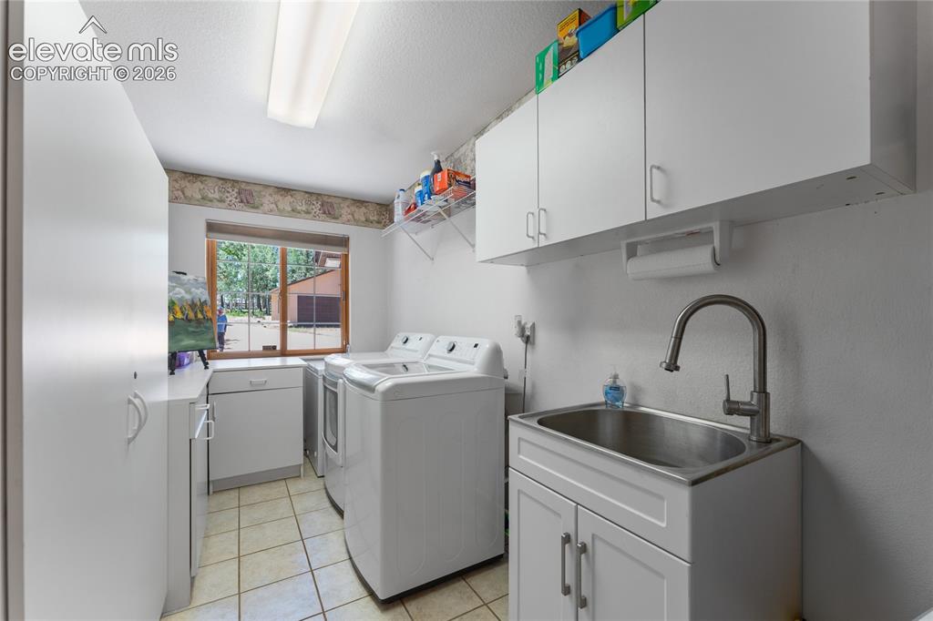 Image 23 of 43: Utility room with white cabinetry, tile flooring, and a stainless steel uti