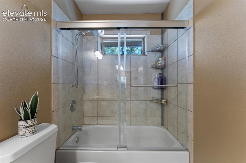 Image 26 of 43: Bathtub with a glass sliding door enclosure, surrounded by light-toned tile