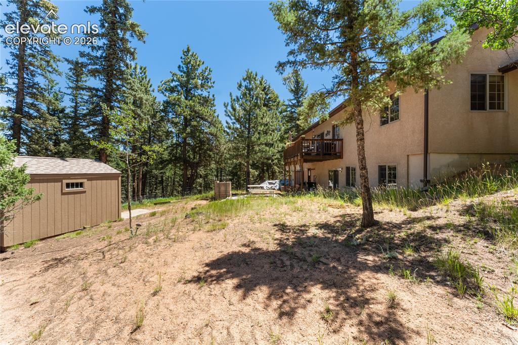 Image 39 of 43: Stucco exterior dwelling with a tiered wooden deck, surrounded by mature pi