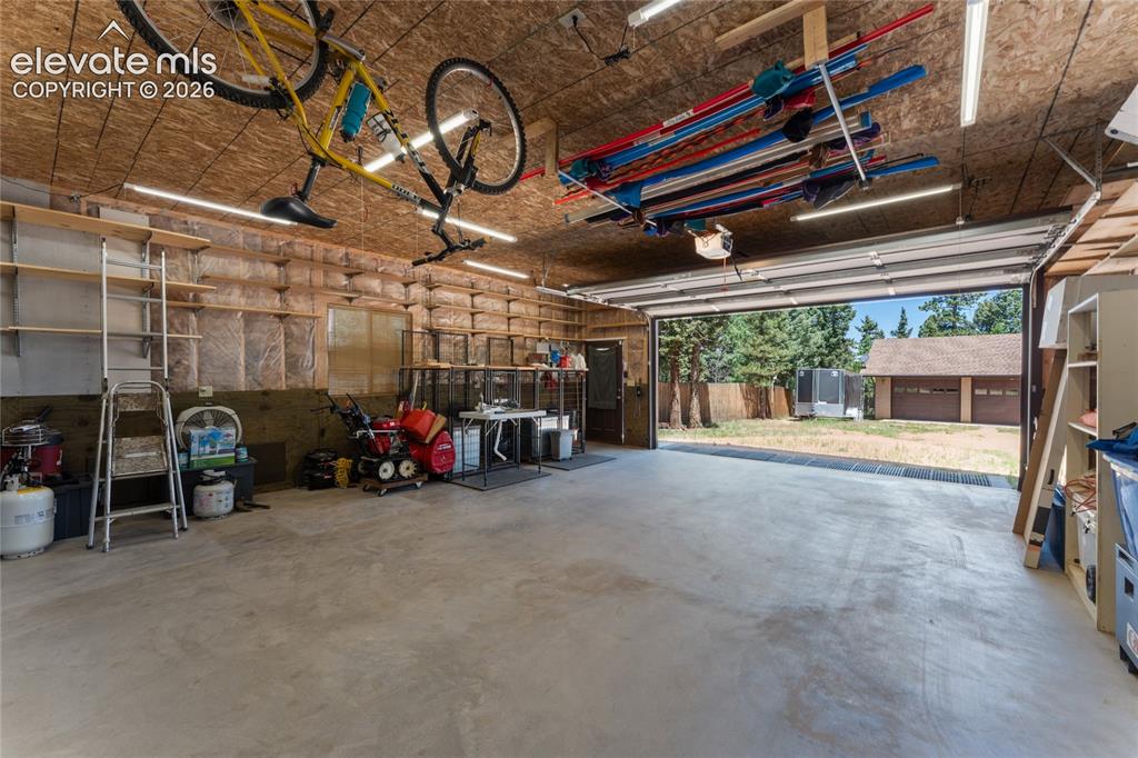 Image 40 of 43: Spacious two-car garage with overhead storage, exposed wood-finish ceiling,