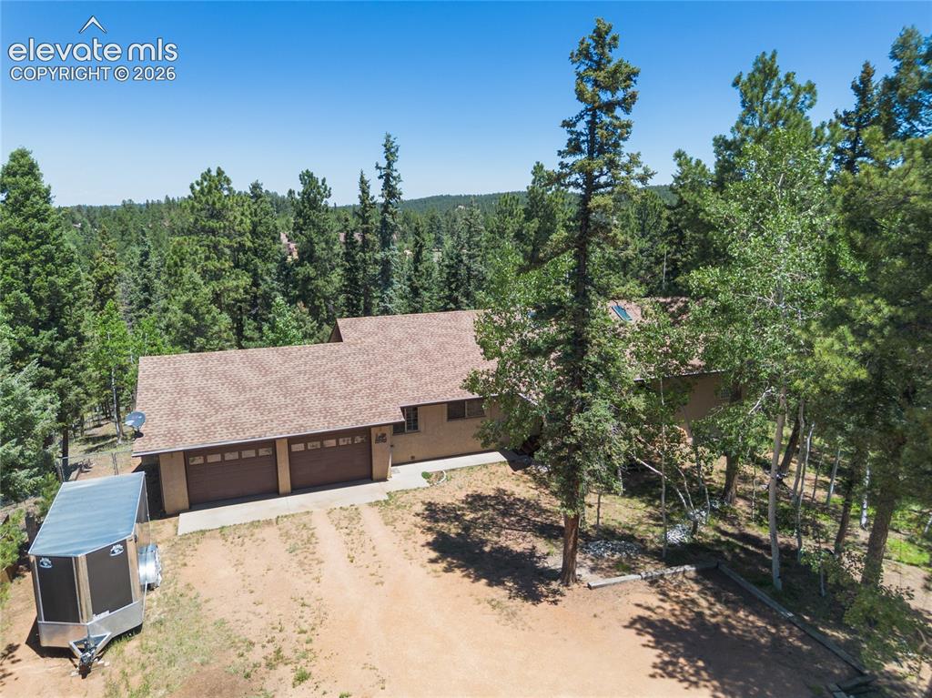 Image 41 of 43: Exterior with a multi-car garage, surrounded by mature trees, and featuring