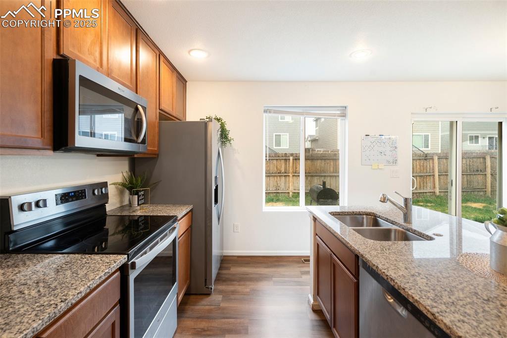 Image 10 of 29: Kitchen featuring light stone counters, a sink, brown cabinets, dark wood f